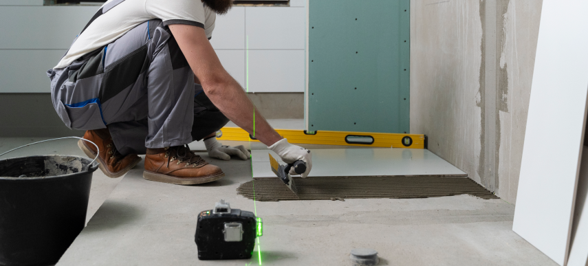 Professional contractor applying mortar with a notched trowel to lay floor tiles during a bathroom remodeling project